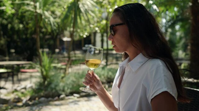 An adult woman a wine connoisseur is relaxing in a bar on the street with a glass of cold white wine during the day at the resort