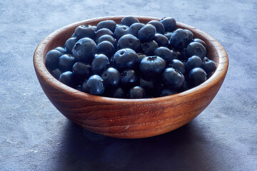 Ripe blueberries in a wooden bowl on a dark background
