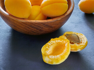 Ripe juicy apricots in a wooden bowl on a dark table