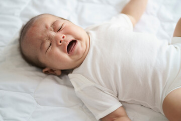 Asian newborn crying baby boy. New born child tired and hungry in bed.Children cry. Bedding for kids. Infant screaming. Healthy little kid shortly after birth.