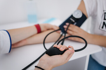 Close-up of doctor using sphygmomanometer with stethoscope checking blood pressure to a female patient in the clicic