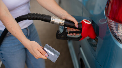 A woman fills her car with gasoline at a self-service gas station and holds a credit card