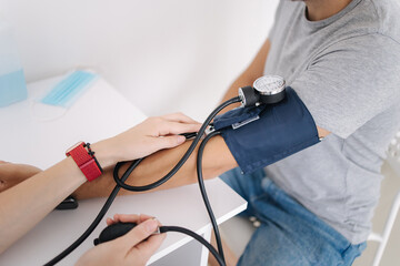 Young man with high blood pressure. Female doctor using sphygmomanometer with stethoscope checking...