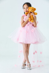 Portrait studio shot of Asian pretty girl wears white princess long rose flower dress fashion costume look at camera and hug fluffy orange teddy bear doll in front white background