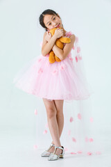 Portrait studio shot of Asian pretty girl wears white princess long rose flower dress fashion costume look at camera and hug fluffy orange teddy bear doll in front white background