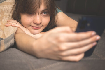 Young girl with mobile phone in hand on sofa with warm plaid. Autumn cozy weekends at home background photo