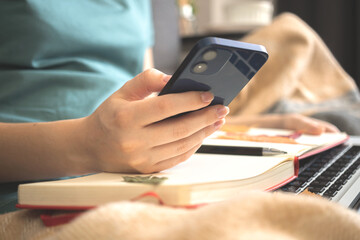 Cozy days at home, autumn weekends with book and mobile phone. Yuog girl holding and using smartphone sitting on sofa with warm plaid