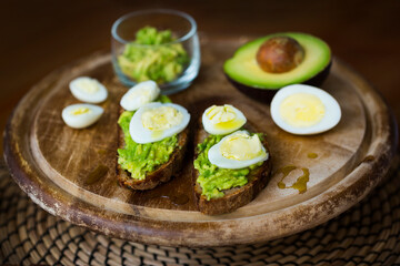 Homemade crostini or sandwich with rye bread, avocado, boiled quail and chicken eggs and olive oil