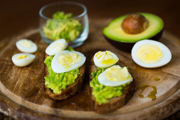 Homemade crostini or sandwich with rye bread, avocado, boiled quail and chicken eggs and olive oil