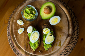 Homemade crostini or sandwich with rye bread, avocado, boiled quail and chicken eggs and olive oil