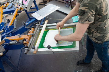 Serigraphy silk screen print process at clothes factory. Frame, squeegee and plastisol color paints.