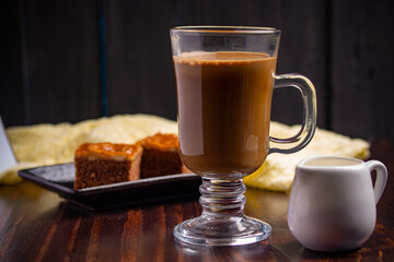 Hot espresso coffee in a clear glass and cakes on wooden background