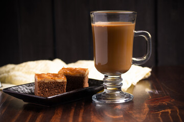 Hot espresso coffee in a clear glass and cakes on wooden background