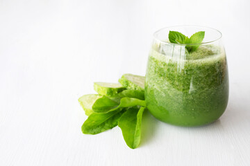 Raw green smoothie with herbs and cucumber on white wooden background.