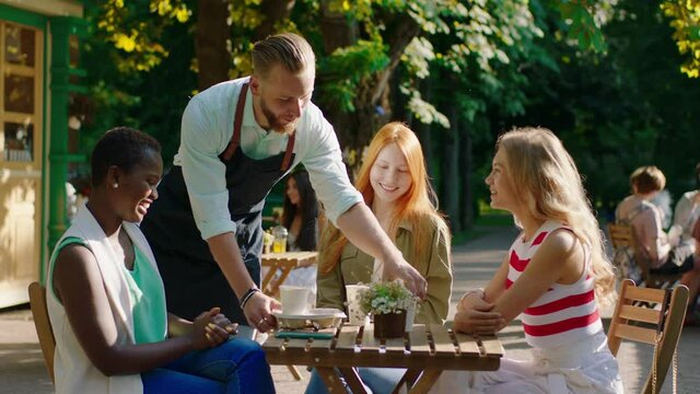 Good looking group of multiracial friends ladies very charismatic enjoy the time at the patisserie barista man brings a fresh coffee for them