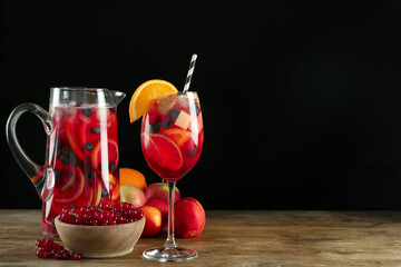 Glass and jug of Red Sangria with fruits on wooden table against black background. Space for text