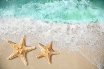Fototapeta na wymiar Beautiful waves and sea stars on sandy beach, top view