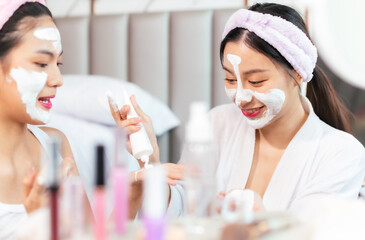 Beautiful young asian woman in white bathrobe applying a revitalizing  mask her friend's face.The woman is applying a face mask on her friends face.