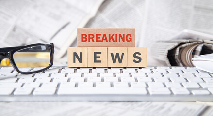 Text Breaking News on wooden cube with a computer keyboard, newspapers and eyeglasses.
