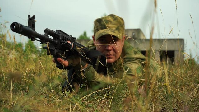 a man taking aim from a machine gun lying in the bushes.