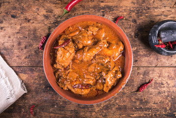 Chicken paprikash in a clay bowl on a wooden table, top view