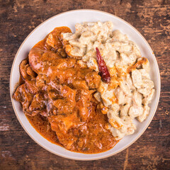 Chicken paprikash with gnocchi or dumplings in a plate on a wooden table, top view, close-up