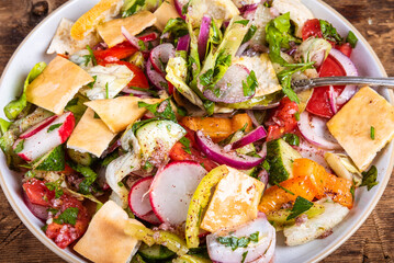 Fattoush arabic vegetable salad with tomatoes, radishes, onions, cucumbers and lettuce in a plate, close-up - rustic style