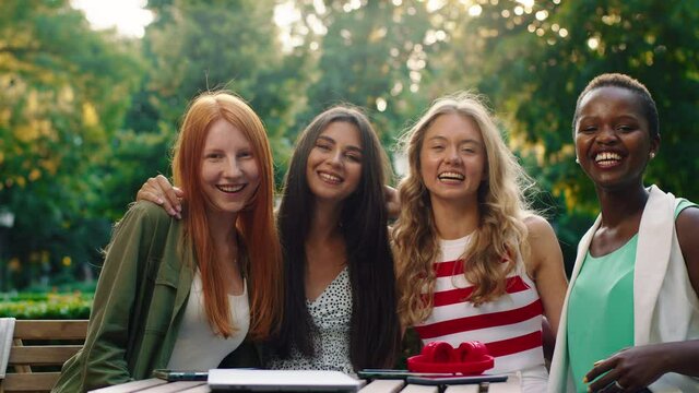 A close up of four friends that are very beautiful sitting at a table outside in the park, laughing and enjoying eachother a company