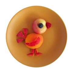 A funny bird made of fruit on a plate. A plate on a white background.