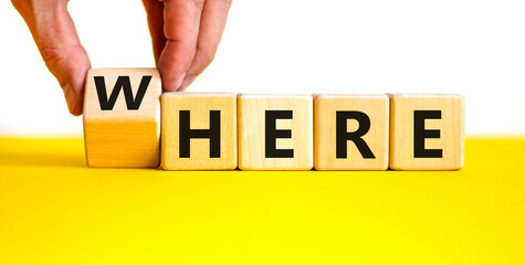 Where or here symbol. Businessman turns a wooden cube, changes the word 'where' to 'here'. Beautiful yellow table, white background, copy space. Business, where or here concept.