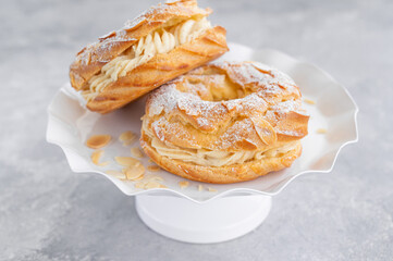 French traditional cake Paris Brest with praline cream, powdered sugar and almond petals on top on a gray concrete background. Copy space.