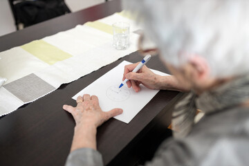 Unrecognizable senior gray-haired woman drawing clock test for dementia, placing numbers in wrong...