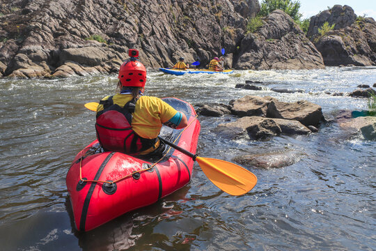 A woman rowing inflatable packraft on whitewater of mountain river. Concept: summer extreme water sport,  active rest, extreme rafting. Back view