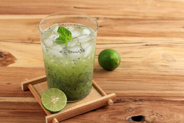 Indonesian Vegetarian Drink Es Timun Serut made from Shredded Cucumber, Lime Juice, and Basil Seeds, Served on Clear Glass on Wooden Table