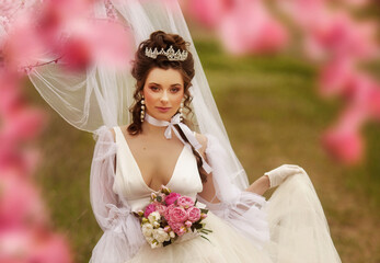 Beautiful bride in a white dress under the sakura tree and flower petals 