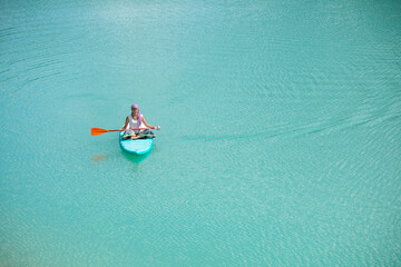 A girl in a dress floats on a glanders board on a pond with bright turquoise water. Warm summer day for travel. 