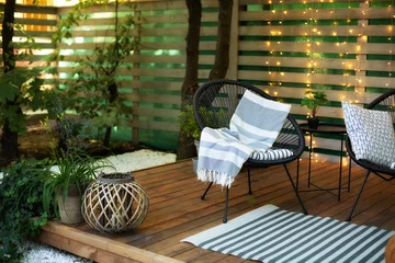 Fotobehang Buitenveranda van huis met zwarte Acapulco fauteuils en plantenpotten. Gezellige ruimte in terras of balkon met guirlande. Interieur Houten veranda met tuinmeubelen. Moderne lounge buiten in de achtertuin © stock_studio