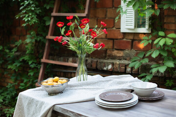 A bouquet of red poppies in a glass vase. Flowers in a vase at home. Interior Terrace, patio. Wooden table and plates for garden party or dinner. Table for lunch outside in garden in yard of house.	