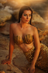 Fototapeta premium Beautiful fashionable mermaid with red hair holding shell sitting on rock near sea
