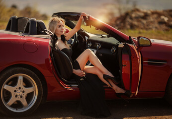 beautiful glamorous girl with white hair in a black elegant long evening dress sits in a convertible