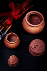 makeup brushes, eyeshadow and blush shimmer in clay pots, on a black background