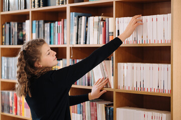 Happy tenage girl or student taking book from shelf in library - People, knowledge, education and school concept