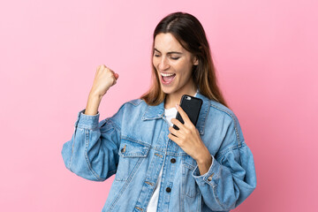 Young caucasian woman isolated on pink background with phone in victory position