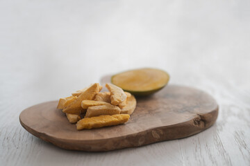 Freeze-dried mango with fresh one on olive wood board with copy space
