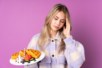 Teenager Russian girl holding waffles isolated on purple background with headache