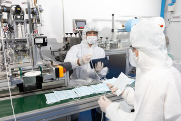 male engineers wearing personal protective equipment uniform(PPE), producing medical face mask beside machine in laboratory