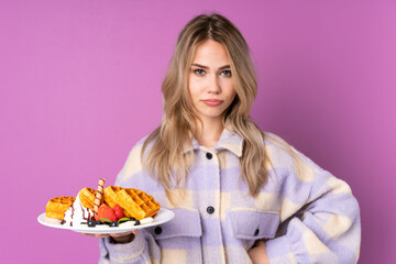 Teenager Russian girl holding waffles isolated on purple background angry