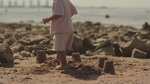 Slowmo shot of African-American toddler boy stomping on sand castles on beach in summer