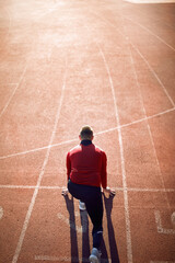 Back view of man  in starting position for running on race track in stadium