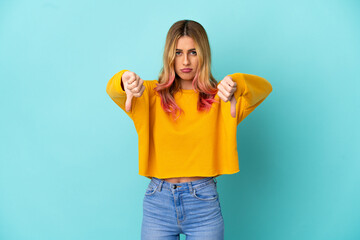 Young woman over isolated blue background showing thumb down with two hands